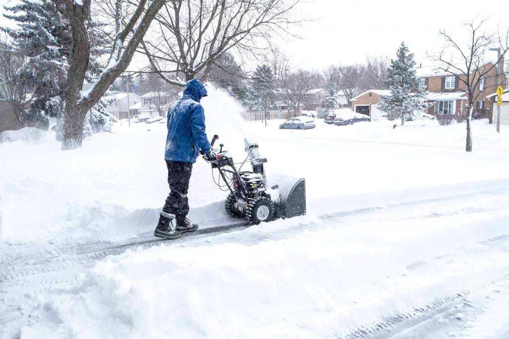 Man in a blue coat Removing Snow With a Snowblower