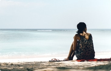 a woman sitting on a a beach looking out at the water